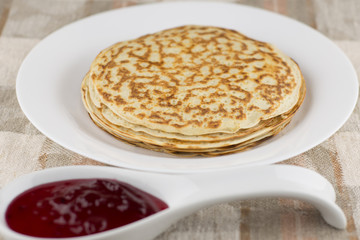 the celebration of carnival: fresh cooked real Russian pancakes made with yogurt, on a white plate and currant jam blurry found. Linen tablecloth, front view, close