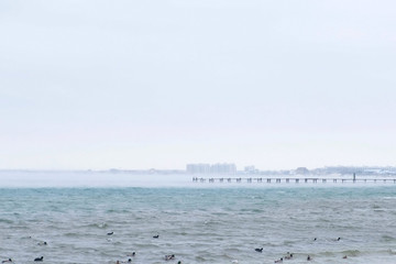 Fog over the sea in the early morning. Beautiful seascape in pastel colors with coastal town on background.