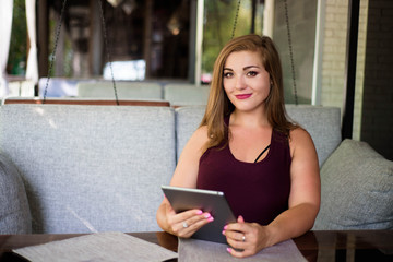 Everyday look. Plus size model. Beautiful young woman with a tablet in a restaurant.