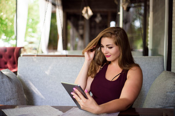 Everyday look. Plus size model. Beautiful young woman with a tablet in a restaurant.