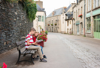 Teenagers travel concept. Children with map sitting on the bench in the street of an old town, historical centre of the town, Rochefort-en-Terre, France