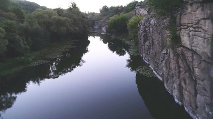 Rough stream flowing between two rocky banks with cane and trees in summer