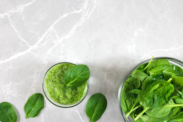 Green healthy spinach smoothie in a  glass, bowl with fresh spinach and spinach leaves on a marble background with copy space.