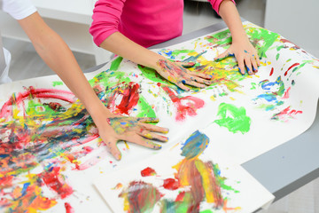 detail closeup of two kids hand painting with color paint on a white paper