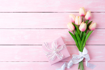 Valentines day and love concept. Pink paper hearts with gift box and tulips with ribbon on pink pastel wooden background.