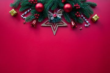 Christmas background concept. Top view of Christmas tree with spruce branches, pine cones, red berries and golden star on red background.