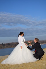 Fototapeta na wymiar Bräutigam kniet mit Blumenstrauß vor seiner Braut am Strand