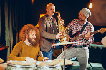 Band practicing for the gig. Musicians playing drums, saxophone and bass guitar. Home studio interior.