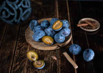 Blaue Zwetschgen auf dunklem Holztisch mit Gewürzen