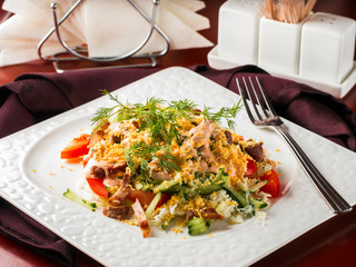 Close up view of salad with bacon, cucumber, pepper and dressed with egg. Salad in white plate on dark brown wooden table in restaurant