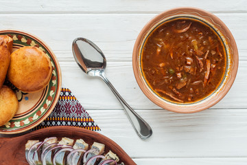 top view of tasty traditional mixed meat soup with mini pies and spoon on white wooden background
