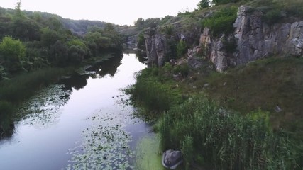 Snaky river running between two rocky banks with lily leaves in summer