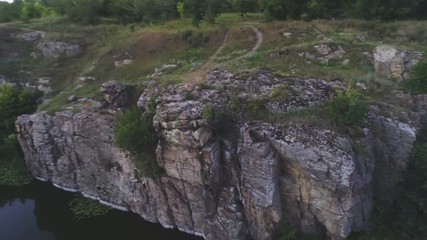 Mountain brook running at a high rocky hill with boulders and trees in summer