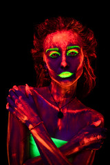 Portrait of a beautiful young sexy girl with ultraviolet paint on her body. Pretty woman with glowing bodyart in black lamp light