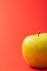 close up view of large golden delicious apple on red background
