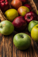 wicker basket with scattered multicolored apples on wooden table