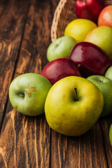 wicker basket with scattered yellow, green and red apples on wooden table