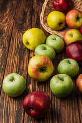 scattered multicolored apples and wicker basket on wooden table