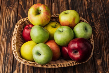 wicker basket with ripe multicolored apples on rustic wooden table