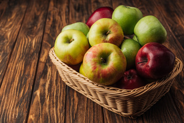 ripe multicolored apples in wicker basket on rustic wooden table