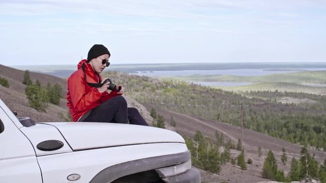 Woman tourist sitting on car at the top of mountain and taking pictures with professional camera