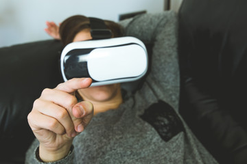 A girl with VR glasses on the couch touching with a finger. Virtual reality glasses