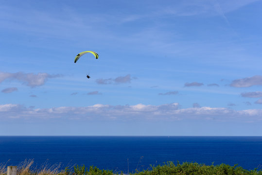 Paragliders against cloudy sky over green countryside