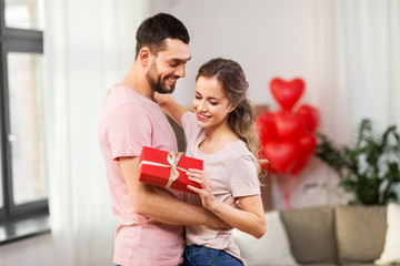 valentines day, relationships and people concept - happy couple with gift box hugging at home