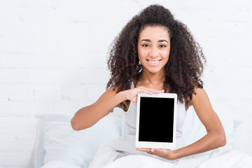 smiling african american woman showing digital tablet with blank screen in bed at home