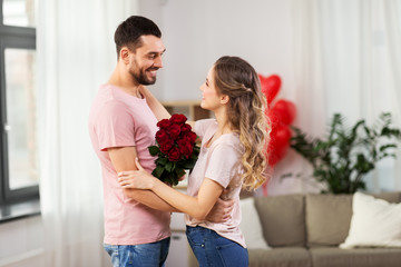 valentines day, relationships and people concept - happy couple with bunch of flowers hugging at home