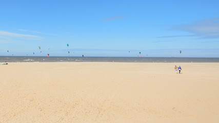 Fototapeta na wymiar Breiter Sandstrand an der Nordseeküste in Scheveningen bei Den Haag, Niederlande - mit Kites von Kitesurfern am Horizont