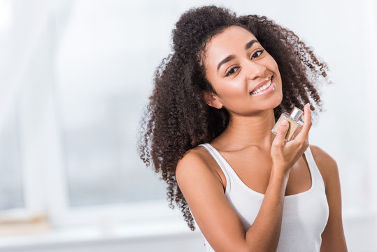 cheerful african american curly girl using perfume at home