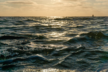 Obraz premium Low view image of waves on the sea at an orange colored sunset and sailing ship on the horizon.