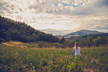 Fototapeta na wymiar Girl sitting on a green meadow and watching the countryside landscape.