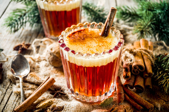 Winter holidays traditional drink, homemade hot buttered rum with spices, over old rustic wooden background with christmas tree branches, copy space
