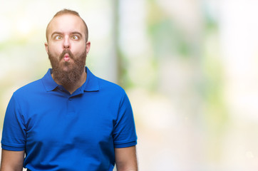 Fototapeta na wymiar Young caucasian hipster man wearing blue shirt over isolated background making fish face with lips, crazy and comical gesture. Funny expression.