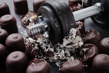 Iron dumbbell dropped in the middle of chocolate covered marshmallows destroying them, diet concept