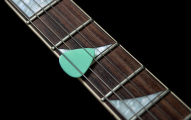 fingerboard of an electric guitar and pick on a black background
