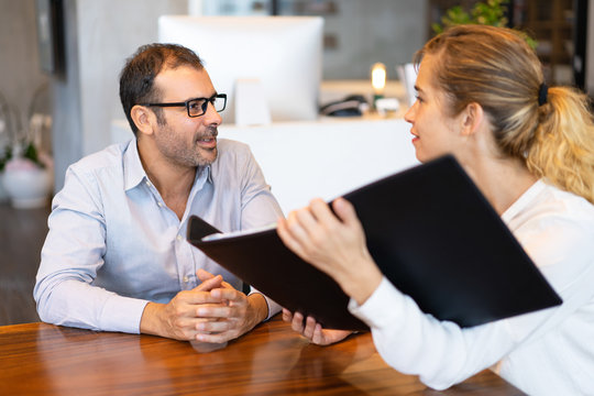 Confident female manager showing her project to male executive. Mid adult businessman wearing glasses having meeting with young partner or colleague. Planning concept