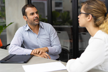 Portrait of serious mid adult hr manager listening to candidate. Young woman sitting at job...