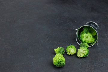a placer of green broccoli cabbages from a small bucket. Template of healthy food on a dark...