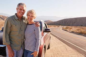 Senior white couple standing on desert roadside by car