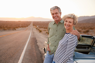 Senior couple on road trip standing by car smiling to camera