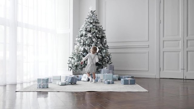 Christmas morning. The room is festively decorated. Kid looks at the Christmas tree