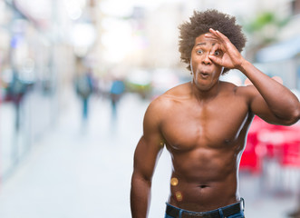 Fototapeta na wymiar Afro american shirtless man showing nude body over isolated background doing ok gesture shocked with surprised face, eye looking through fingers. Unbelieving expression.