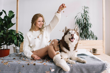 Happy girl and husky sitting on the bed at cozy home. Sexy woman with beautiful body and long legs celebration success. Party time. Elegant smiling female playing with cute adorable dog in bedroom.  © Oleksii