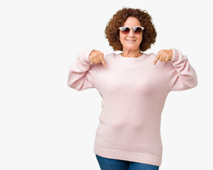 Beautiful middle ager senior woman wearing pink sweater and sunglasses over isolated background...