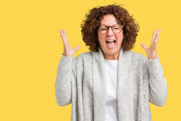 Beautiful middle ager senior woman wearing jacket and glasses over isolated background celebrating mad and crazy for success with arms raised and closed eyes screaming excited. Winner concept