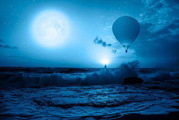 Hot air balloon over the stormy sea against super blue full moon and lighthouse at night