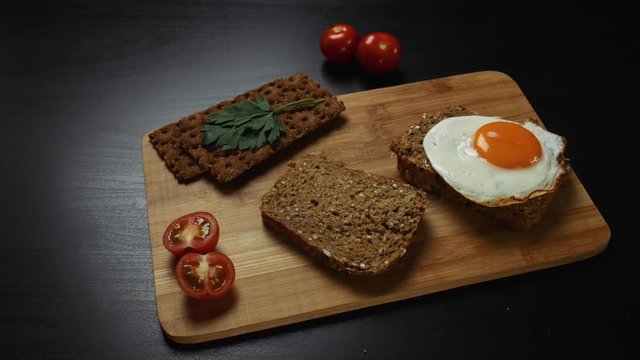 Healthy breakfast. A man is putting scrambled eggs on a fresh grain bread. There are ripe cherry tomatoes, bread crips with parsley on the cutting board
